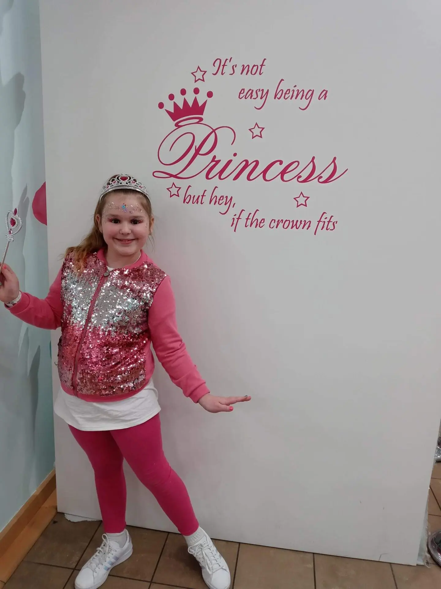 A little girl standing in front of a wall with a princess quote on it.