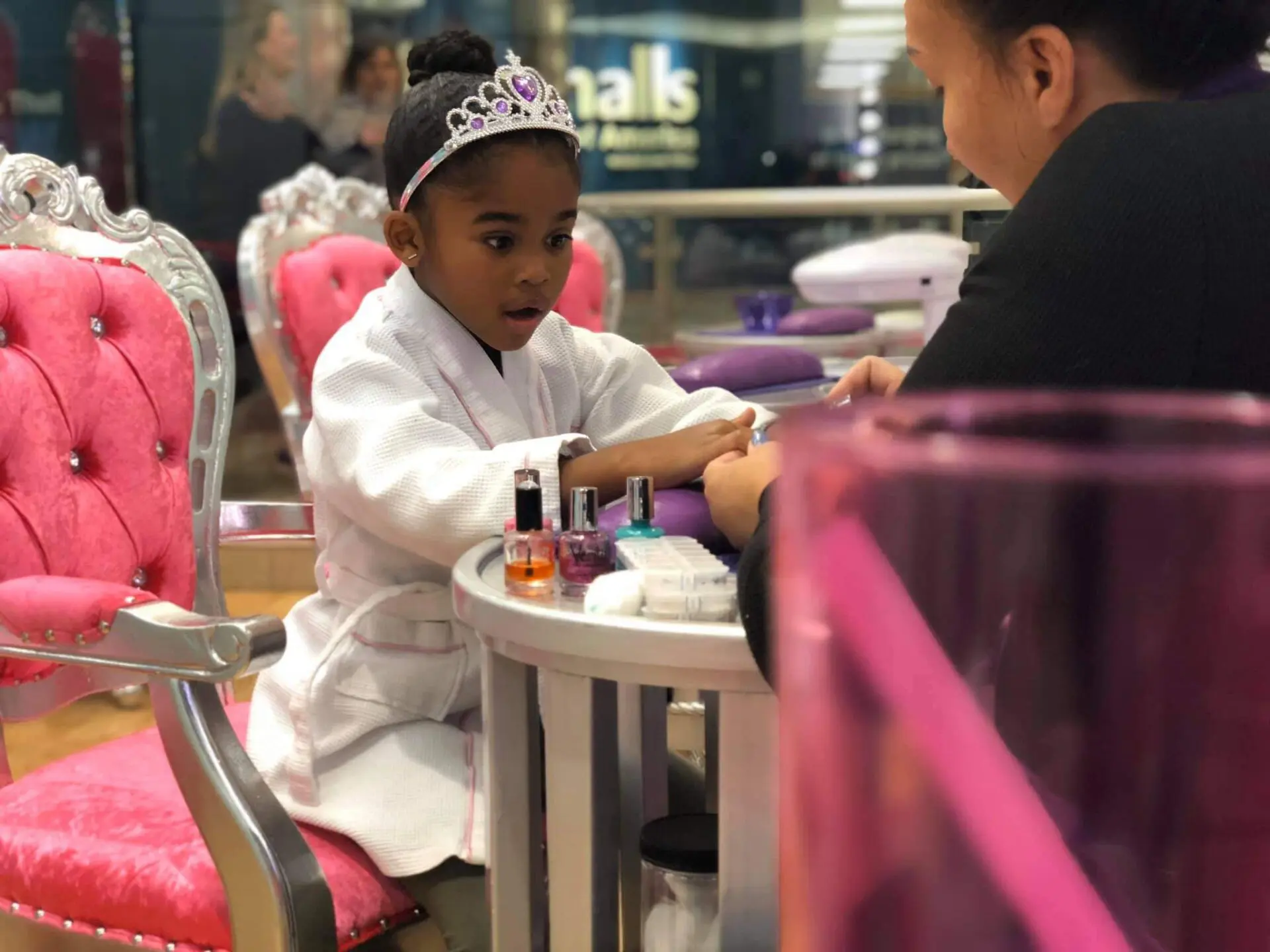 A young girl in a tiara sits at a table with her mother.