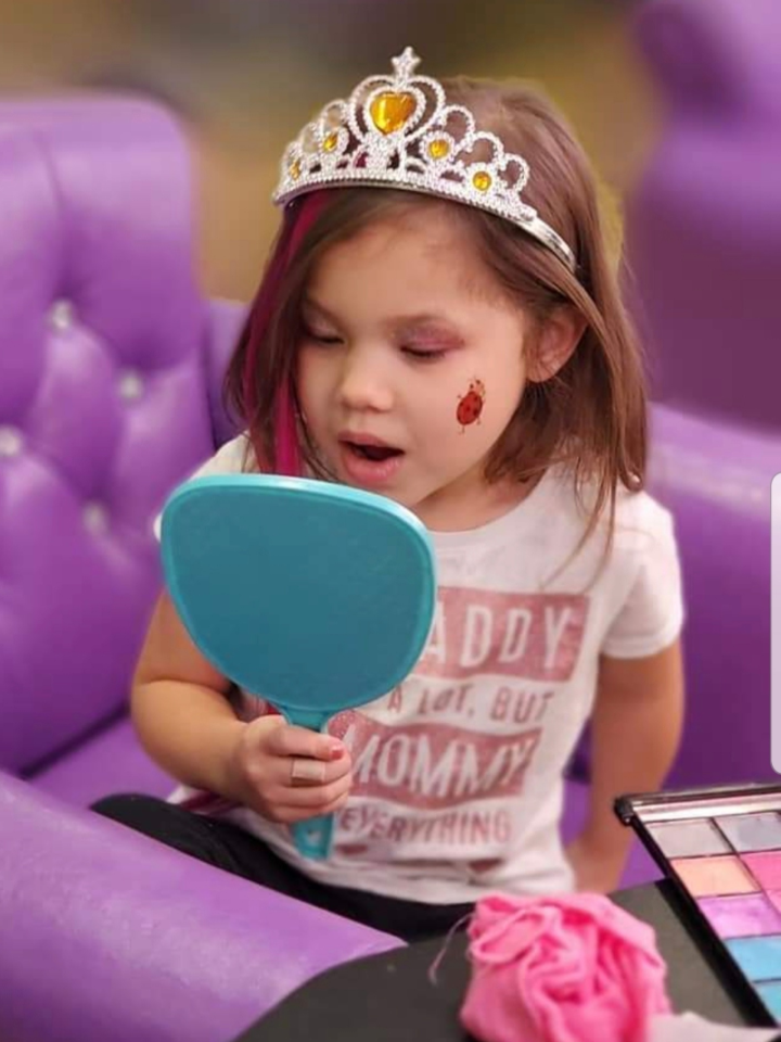 A little girl with a tiara on her head holding a mirror.